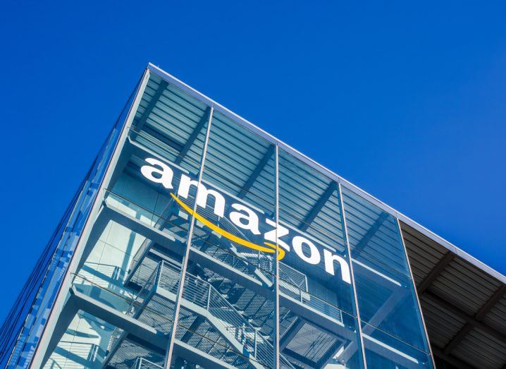 Amazon logo seen on a tall glass building under a blue sky.