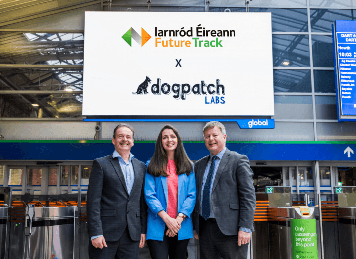 Two men and a woman stand in a railway station with a board behind them that has the Dogpatch Labs and Iarnród Éireann logos on it.