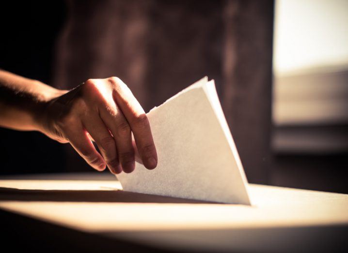 A person putting a piece of paper in a ballot box. Used for the concept of AI and its impact on elections.