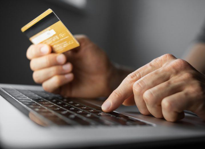 A person's hands typing on a keyboard while holding a debit card.
