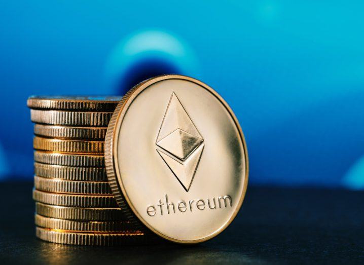 A gold coin with the Ethereum logo on it, next to a small pile of coins.