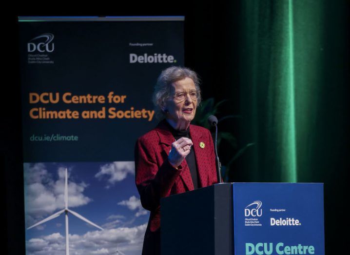 Mary Robinson stands speaking at a podium at a climate conference. She is wearing a red coat.