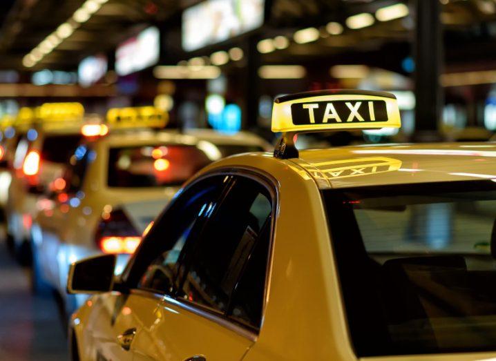 Many taxis parked in a taxi line.