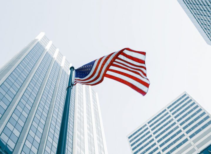 The US flag hoisted in the middle of many tall buildings.