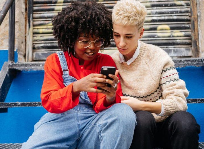 Two teenagers look at a smartphone screen.