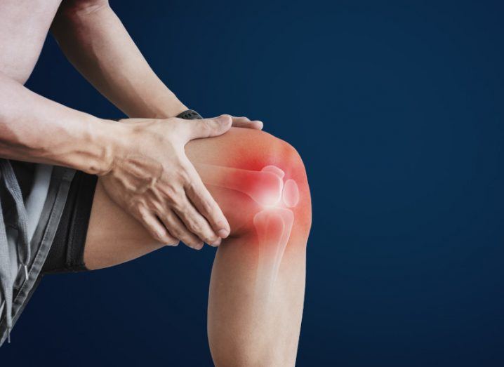 A man holding his knee with an illustration of his joints and muscles visible.