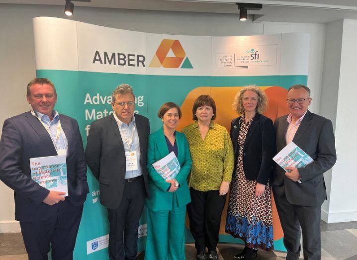 Three men and three women standing together in front of a sign with the Amber logo on it.