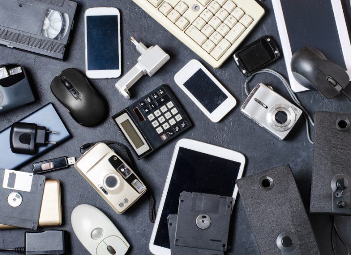 A bunch of different electrical items such as phones, keyboards and cameras, scattered across a charcoal surface, symbolising fast tech and e-waste.