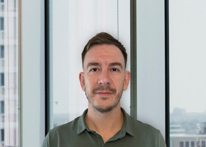 A headshot of Marc Wren against a glass window with a city skyline in the background.